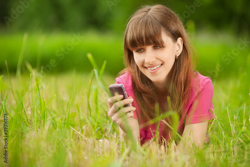 Photo: Young woman with mobile phone lies on green grass Young woman with mobile phone lies on green grass