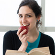 Portrait of a pretty young student eating an apple while reading