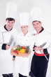 Three smiling chefs holding vegetable board