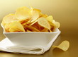 potato chips in a white bowl on a gold background potato chips in a white bowl on a gold background