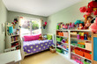 Girls bedroom with many toys and purple bed.