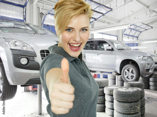 Photo: Young woman shows thump up in a garage after tyre changing Young woman shows thump up in a garage after tyre changing