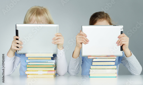 Foto: Two pupils leaning on a pile of books while reading on touchpad Two pupils leaning on a pile of books while reading on touchpad