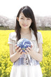 菜の花畑で地球儀を持つ笑顔の女性