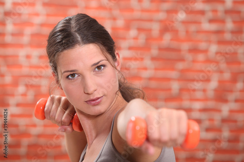 Photo: Young woman using hand weights in front of a red brick wall Young woman using hand weights in front of a red brick wall