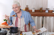 Elderly woman cooking dinner with the help of a recipe