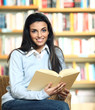 smiling female student with book in hands sitting in a chair in
