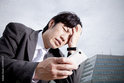 Photo: スマートフォンを見て頭を抱えるビジネスマン スマートフォンを見て頭を抱えるビジネスマン