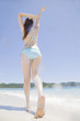 伸びをしながら波打ち際を歩く水着女性の後姿