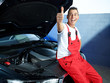 Happy apprentice in a garage sitting on a car shows thumb up