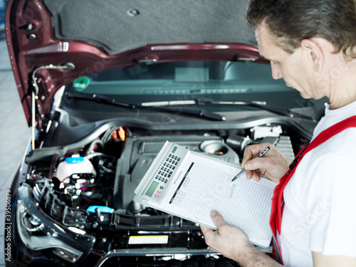 Foto: Motor mechanic in front engine bay writing a quotation Motor mechanic in front engine bay writing a quotation