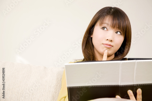 Photo: ソファに座り本を見ながら考え事をしている女性 ソファに座り本を見ながら考え事をしている女性