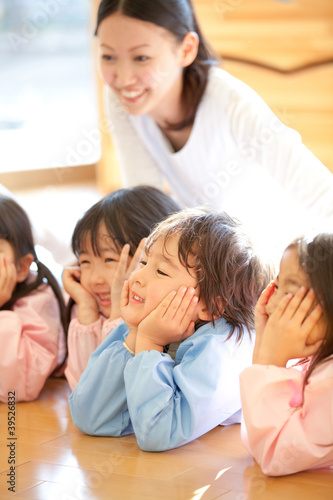 Photo: 頬杖をついて微笑む幼稚園児と笑顔の幼稚園教諭 頬杖をついて微笑む幼稚園児と笑顔の幼稚園教諭
