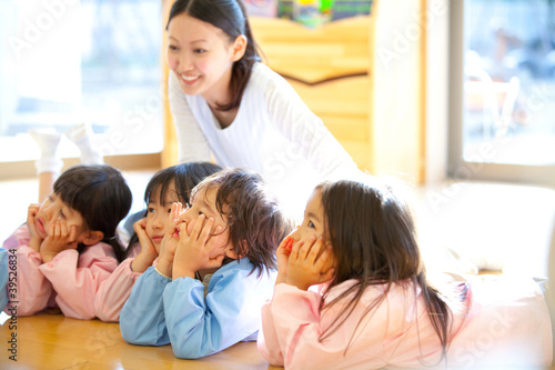 Photo: 頬杖をついて微笑む幼稚園児と笑顔の幼稚園教諭 頬杖をついて微笑む幼稚園児と笑顔の幼稚園教諭