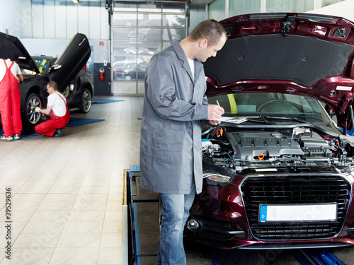 Foto: Master mechanic checking the engine bay, workers in background Master mechanic checking the engine bay, workers in background