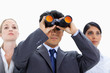Businessman looking up through binoculars with two girls behind him