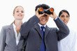 Close-up of a businessman looking up through binoculars with two smiling girls behind him 