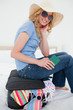 Photo: Close up, woman sitting on a suitcase while smiling and wearing a hat and glasses Close up, woman sitting on a suitcase while smiling and wearing a hat and glasses