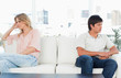 Foto: Man and woman sitting at opposite ends of then couch, both looking upset Man and woman sitting at opposite ends of then couch, both looking upset