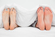 Two pairs of feet, in bed beside each other pointing straight up
