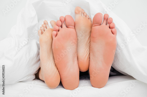 Photo: Two pairs of feet crossed over each other in bed Two pairs of feet crossed over each other in bed