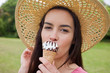 Young woman standing in a park while wearing a hat and eating an ice cream