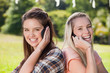 Young smiling women talking on the phone while standing back to back