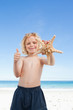 Smiling boy on the beach with starfish giving thumb up