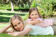 A mother lying on the grass with head in her hands as her daughter lies on her