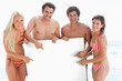 Photo: Four friends smiling and pointing at a blank poster which they hold between them Four friends smiling and pointing at a blank poster which they hold between them