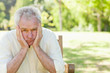 Man looks ahead while holding his face in his hands as he sits on a bench