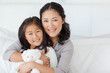 Photo: A daughter and her mom embrace one another on the bed as the child holds a teddy A daughter and her mom embrace one another on the bed as the child holds a teddy