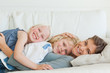 The mother lies across the couch with her son and daughter on top of her