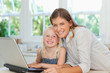 Mother and daughter smiling as they sit together by the laptop