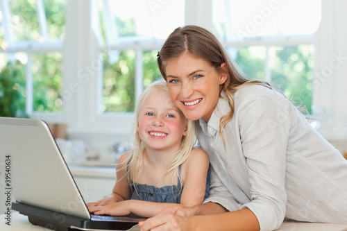 Photo: Mother and daughter smiling as they sit together by the laptop Mother and daughter smiling as they sit together by the laptop