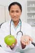 Relaxed doctor holding a green apple and vitamins