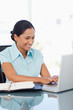 Foto: Smiling woman working with a laptop while sitting at a desk Smiling woman working with a laptop while sitting at a desk