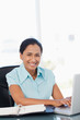 Foto: Smiling secretary typing on her laptop while looking at the camera Smiling secretary typing on her laptop while looking at the camera