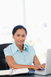 Foto: Calm young secretary working with her laptop while looking at the camera Calm young secretary working with her laptop while looking at the camera