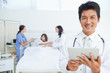 Photo: Doctor smiling while holding a tablet as he stands in front of his colleagues Doctor smiling while holding a tablet as he stands in front of his colleagues