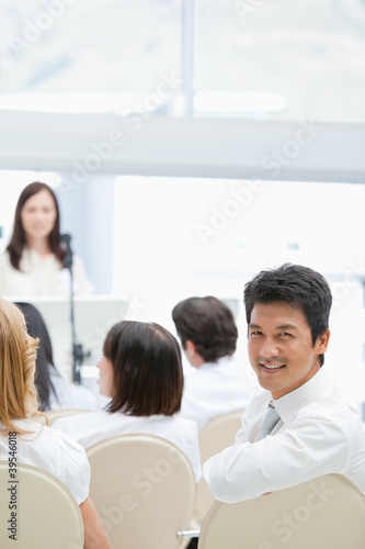 Photo: Businessman smiling while looking behind him during a speech Businessman smiling while looking behind him during a speech