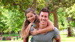 Woman jumps onto her friends back for a piggy-back before they look at the camera while smiling