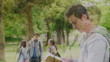 Video: Man reading a book before looking at the camera while smiling as he stands in a park Man reading a book before looking at the camera while smiling as he stands in a park
