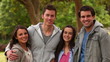 Video: Man holds his three friends and looks at the camera as they stand in a park Man holds his three friends and looks at the camera as they stand in a park