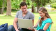 Video: Two friends laughing and talking while looking at a laptop as they sit in a park Two friends laughing and talking while looking at a laptop as they sit in a park
