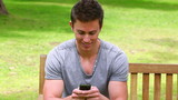 Video: Man sits on a bench while looking at at his mobile phone before laughing and looking at camera Man sits on a bench while looking at at his mobile phone before laughing and looking at camera