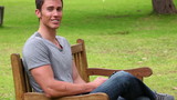 Video: Man looking at his phone while sitting with his legs crossed before looking at the camera Man looking at his phone while sitting with his legs crossed before looking at the camera