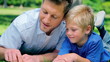 Video: Father talking to his son and pointing to the ground as they lie in the grass Father talking to his son and pointing to the ground as they lie in the grass