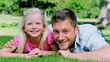 Video: Man looks at his daughter with a confused look before smiling as they lie on the grass Man looks at his daughter with a confused look before smiling as they lie on the grass