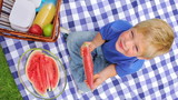 Video: Overhead shot of a boy sitting on a picnic blanket while eating a slice of watermelon and smiling Overhead shot of a boy sitting on a picnic blanket while eating a slice of watermelon and smiling